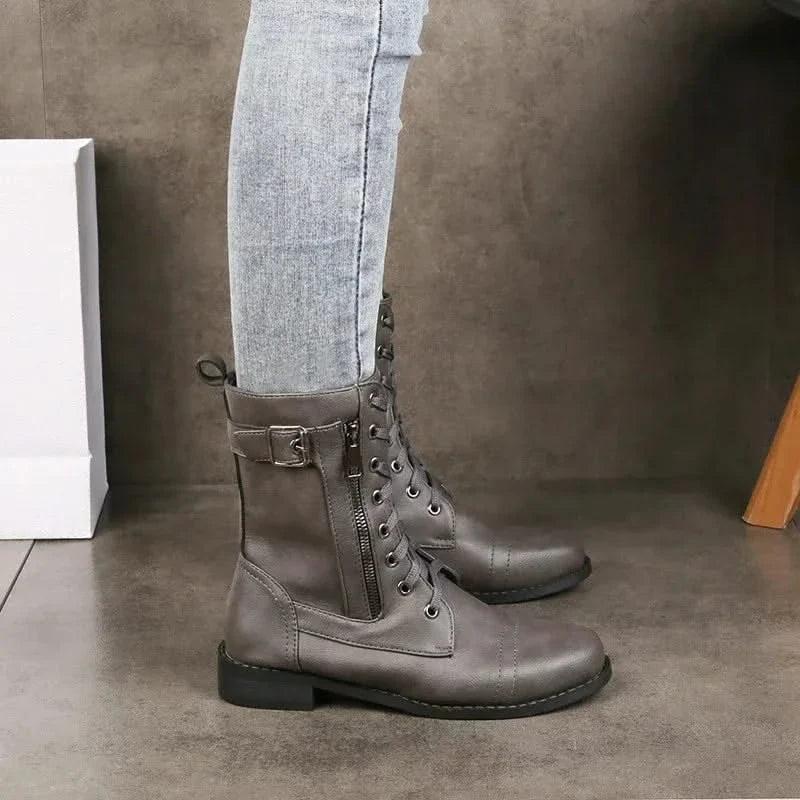 Gray leather lace-up ankle boots with buckled straps worn with light gray jeans.