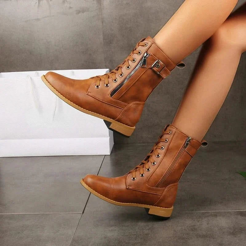 Brown leather lace-up knee-high boots with buckled straps worn by a woman.
