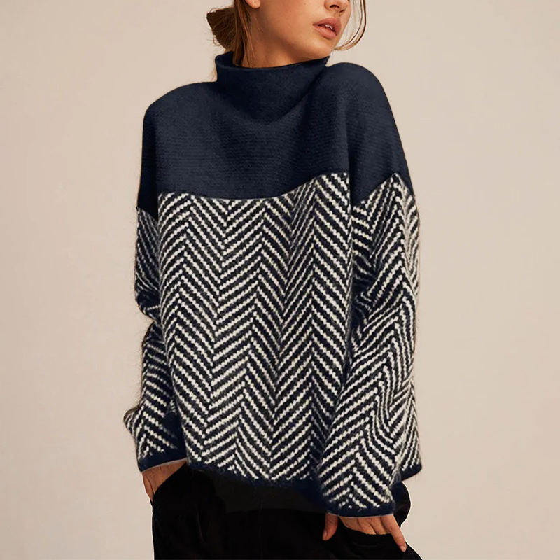 Woman wearing a navy and charcoal color-block knit sweater featuring a mock neck, herringbone knit pattern, and relaxed silhouette.