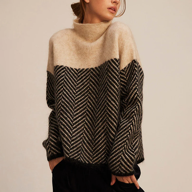 Woman wearing a beige and charcoal color-block knit sweater with a mock neck, herringbone pattern, long sleeves, and a relaxed fit.