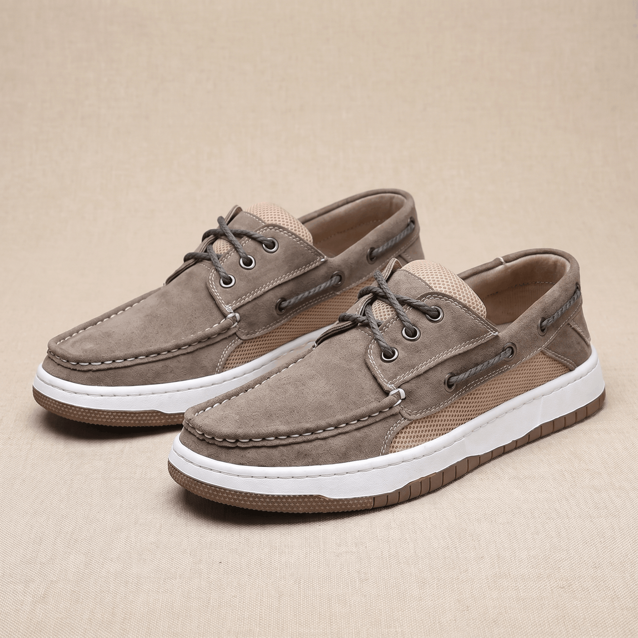 Pair of gray suede Adrian boat shoes with tan mesh panels, placed side by side on a beige surface