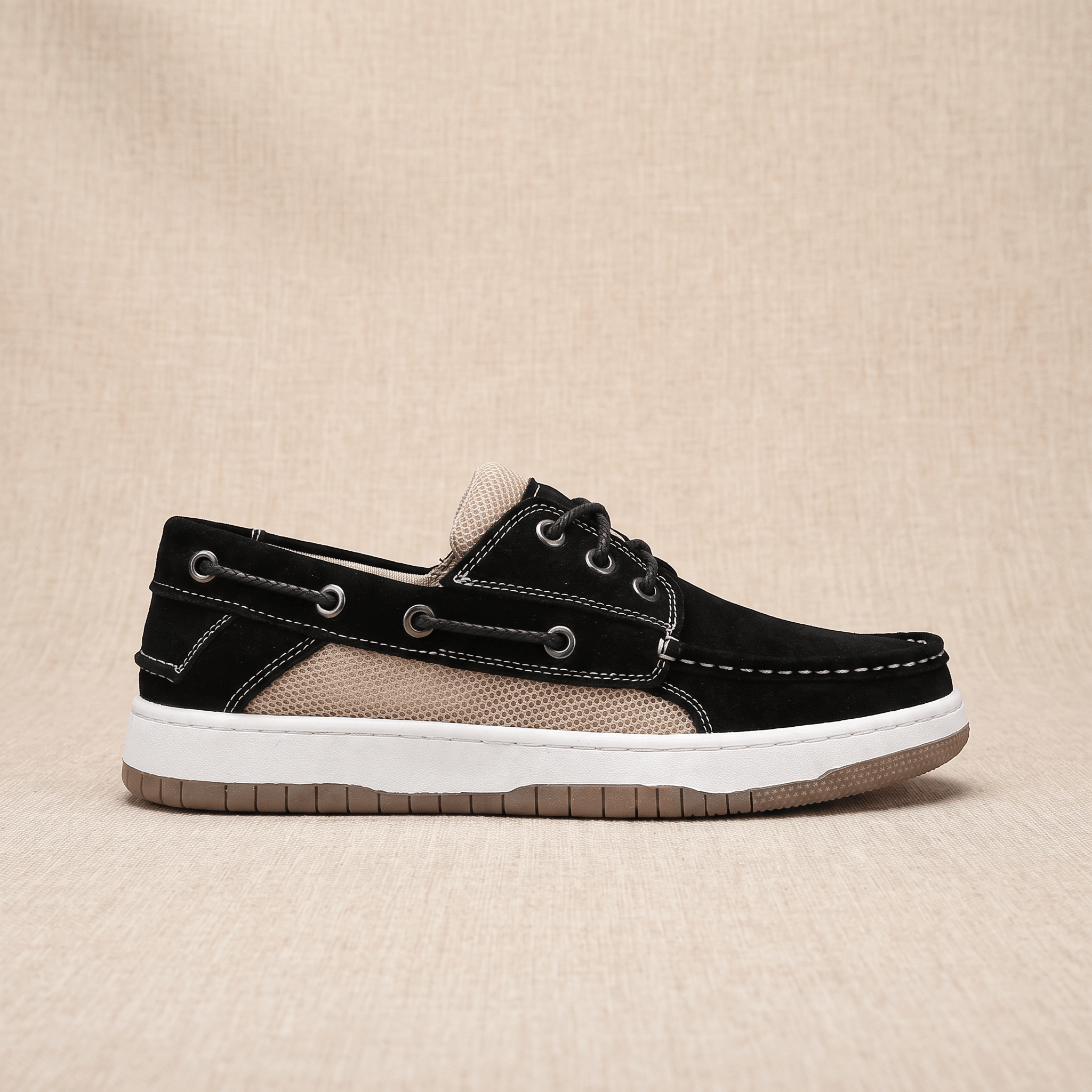 Side profile view of a single black suede Adrian boat shoe showing the beige mesh panel and tan sole