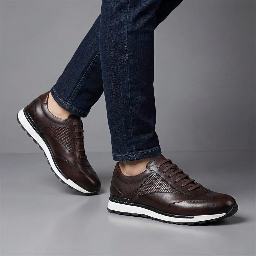 Front-facing view of a person mid-stride wearing dark brown leather sneakers and blue jeans on a gray background.