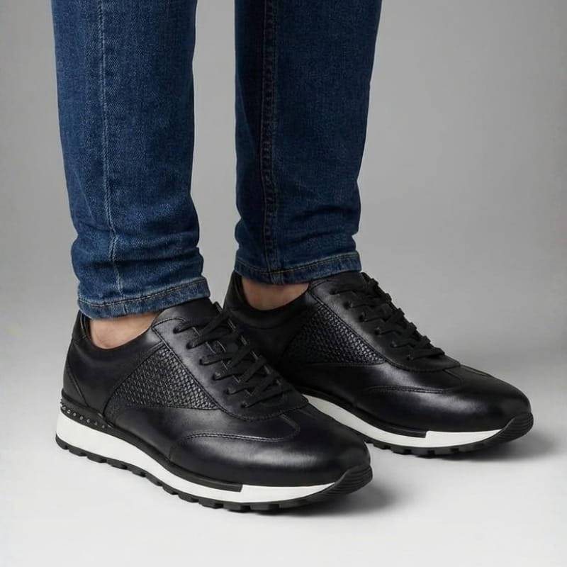 Front-facing view of a person standing in black leather sneakers and blue jeans on a light-colored floor.