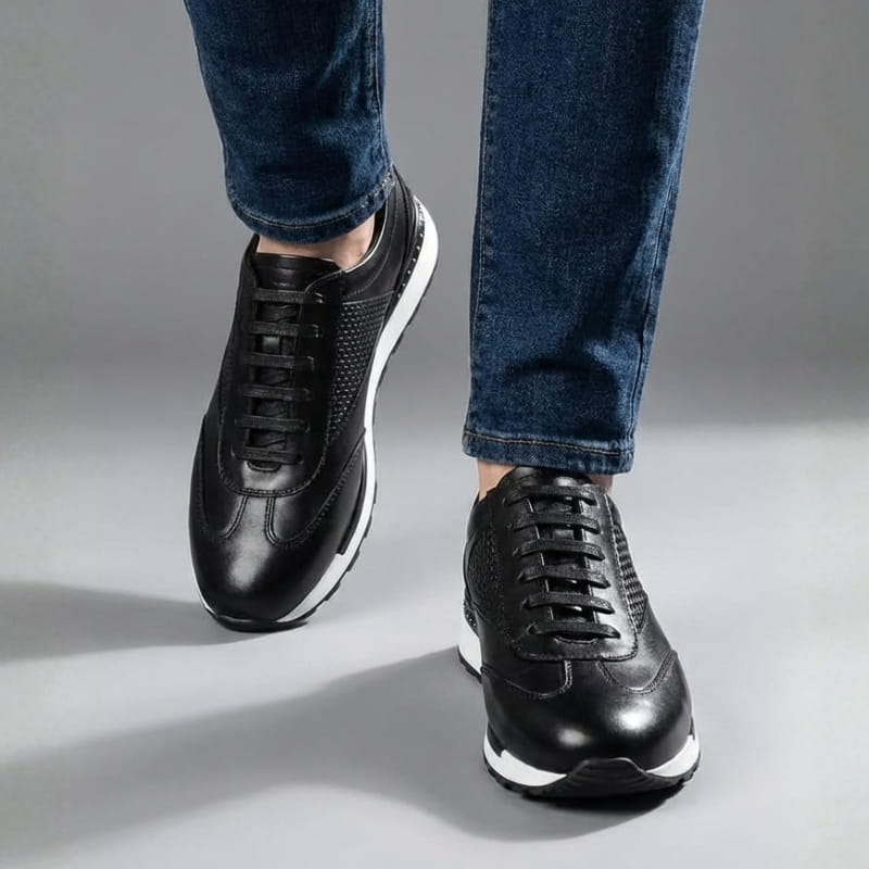 Close-up of a person mid-stride wearing black leather sneakers and blue jeans against a gray background.