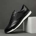 A single black leather sneaker with a woven texture panel and white sole, propped against a concrete block.