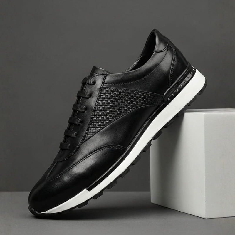 A single black leather sneaker with a woven texture panel and white sole, propped against a concrete block.