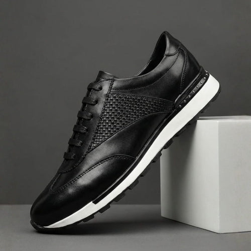 A single black leather sneaker with a woven texture panel and white sole, propped against a concrete block.