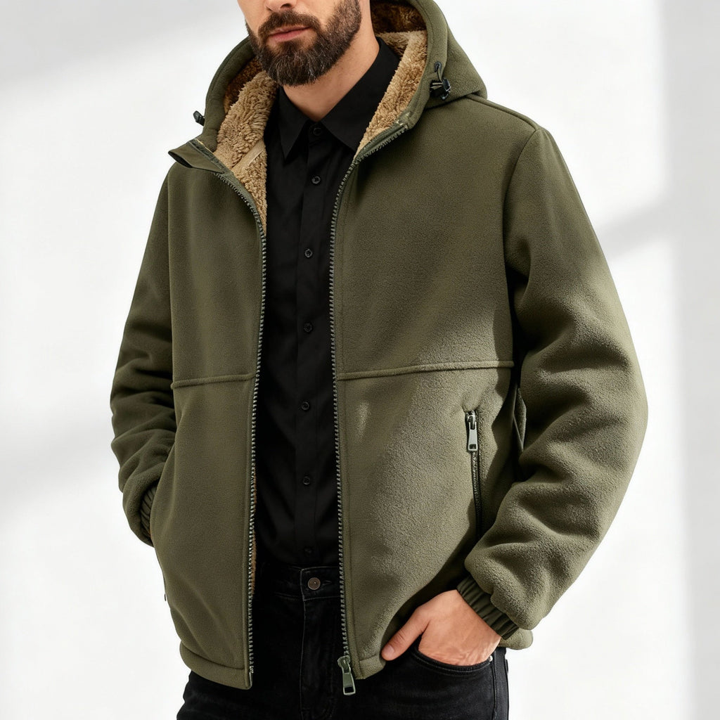 Man wearing an olive green jacket with a sherpa-lined collar, full front zip closure, zippered pockets, long sleeves, and relaxed fit over a black shirt.