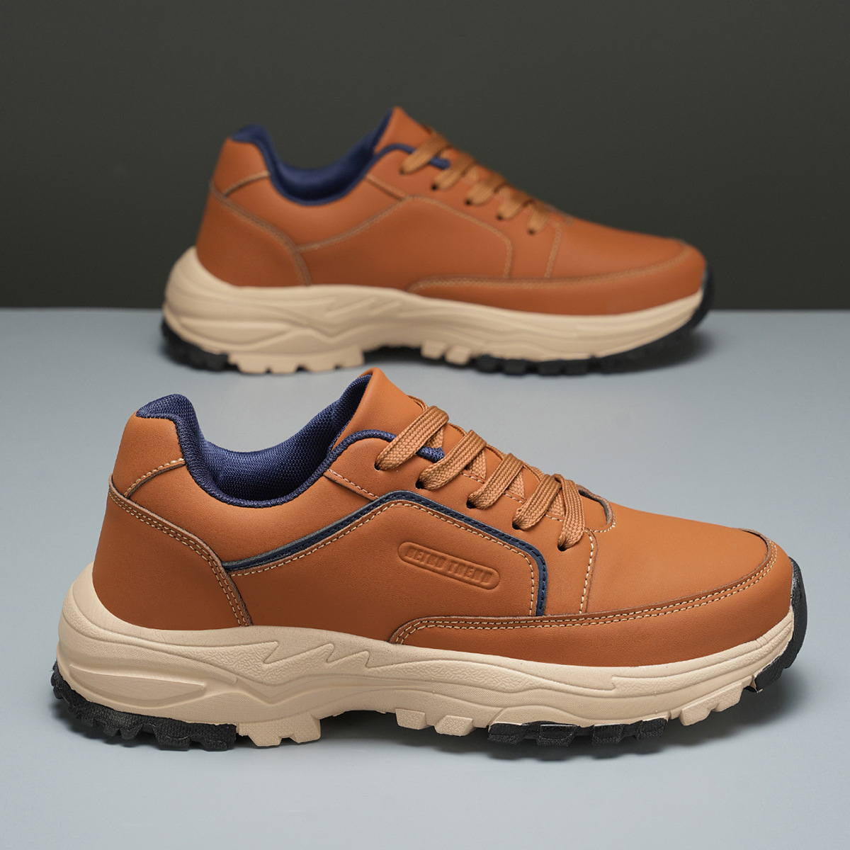 Tan leather Arnold trainers tilted on their side against a two-tone olive and gray backdrop, highlighting the cream tread sole