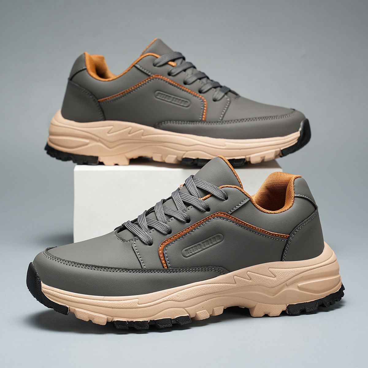 Pair of gray leather Arnold trainers with orange trim and tan sole, one shoe propped upright on a white block