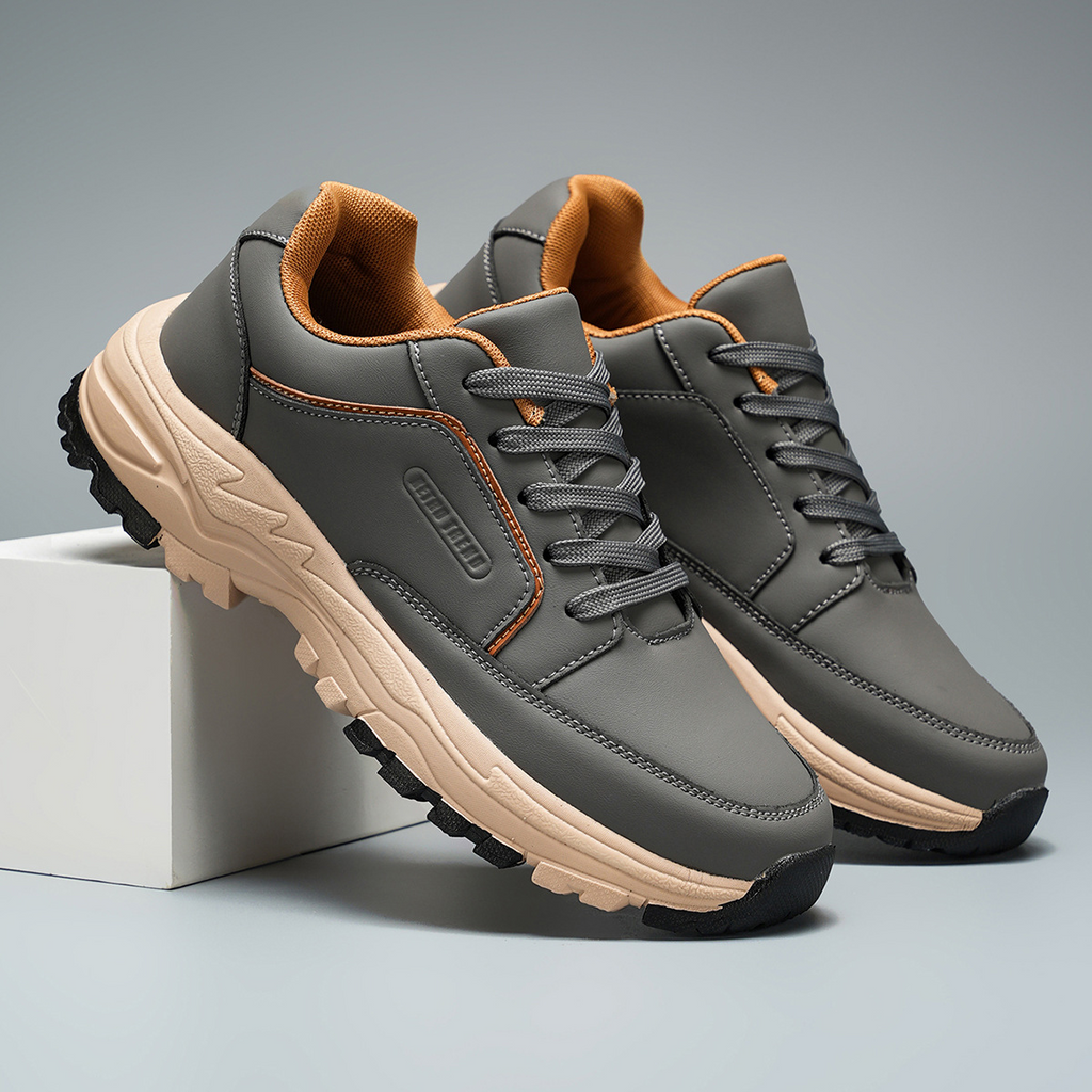 Close-up of two gray leather Arnold trainers with orange collar lining leaning together against a white block