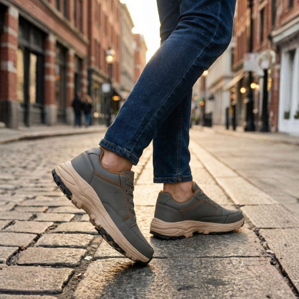 Man walking down a cobblestone street in gray leather Arnold trainers and cuffed jeans, mid-stride with one foot lifted