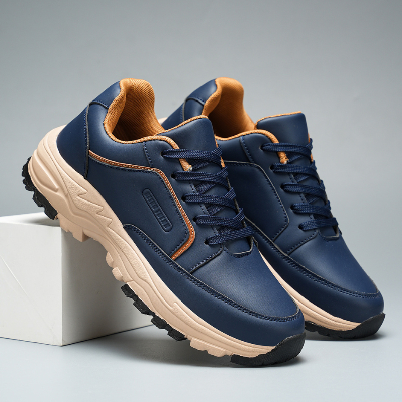 Side angle of navy blue Arnold leather trainers leaning against a white block, showing tan sole and lace-up front