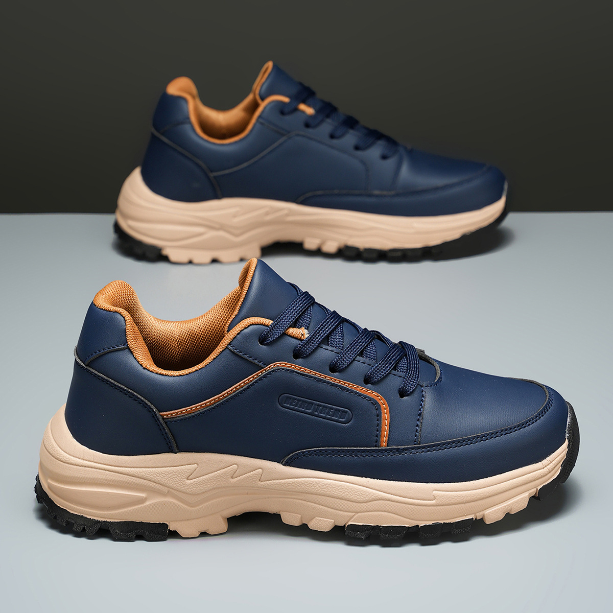 Navy blue Arnold trainers tilted on their side against a two-tone olive and gray backdrop, highlighting the tan tread sole