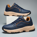 Pair of navy blue leather Arnold trainers with tan cushioned sole and orange trim accents, one shoe propped upright on a white block