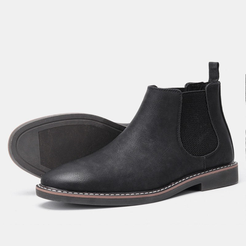 Pair of black leather Chelsea boots, one tilted on its side to show the tread sole, on a plain white background.