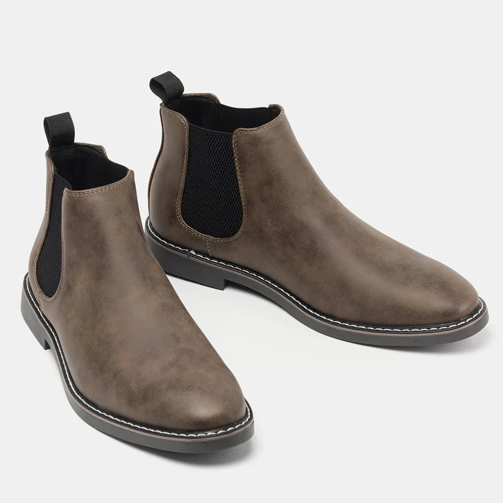 Pair of taupe leather Chelsea boots with elastic side panels, one boot tilted forward, on a plain white background.