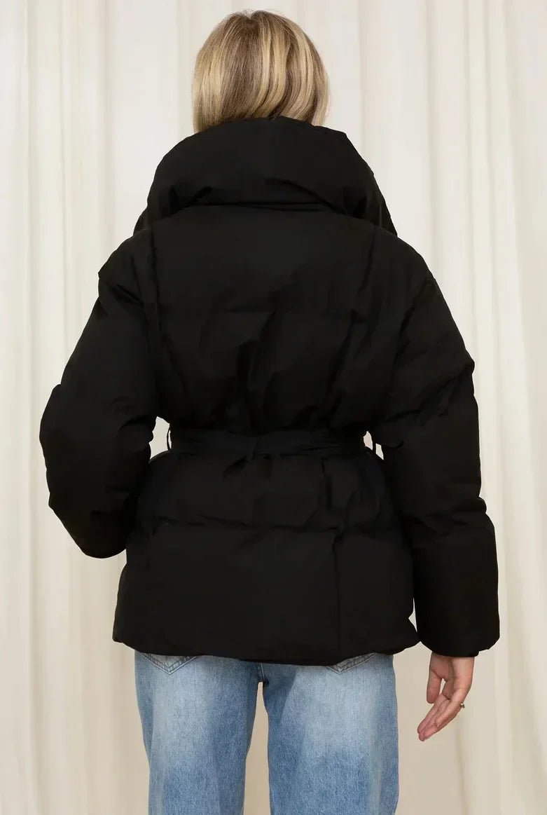 Black quilted puffer jacket with an oversized fit, high stand collar, and a self-tie waist belt worn over blue jeans.