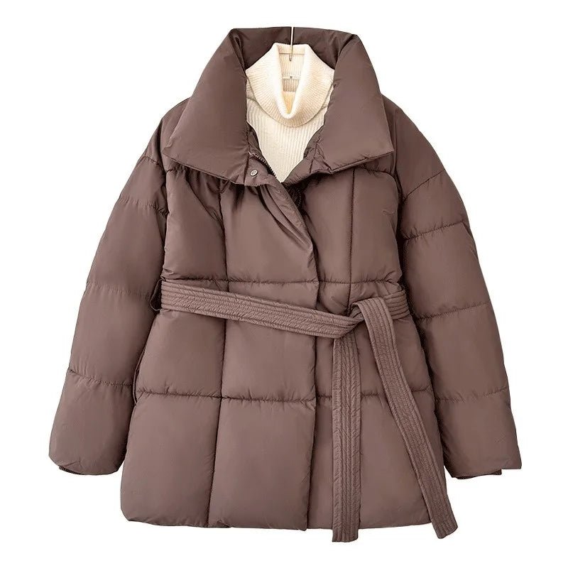 Brown quilted puffer jacket with an oversized fit, high stand collar, and a self-tie waist belt over a cream turtleneck.