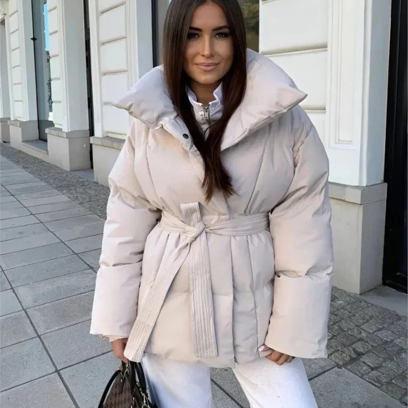 Oversized cream quilted puffer jacket with a high stand collar and self-tie waist belt worn over white trousers.