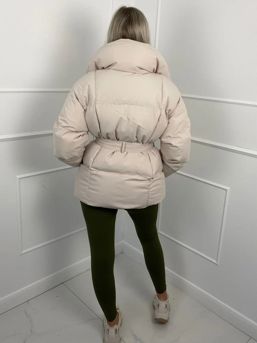 Beige oversized puffer jacket with a high stand collar and cinched waist belt, worn over olive green leggings.