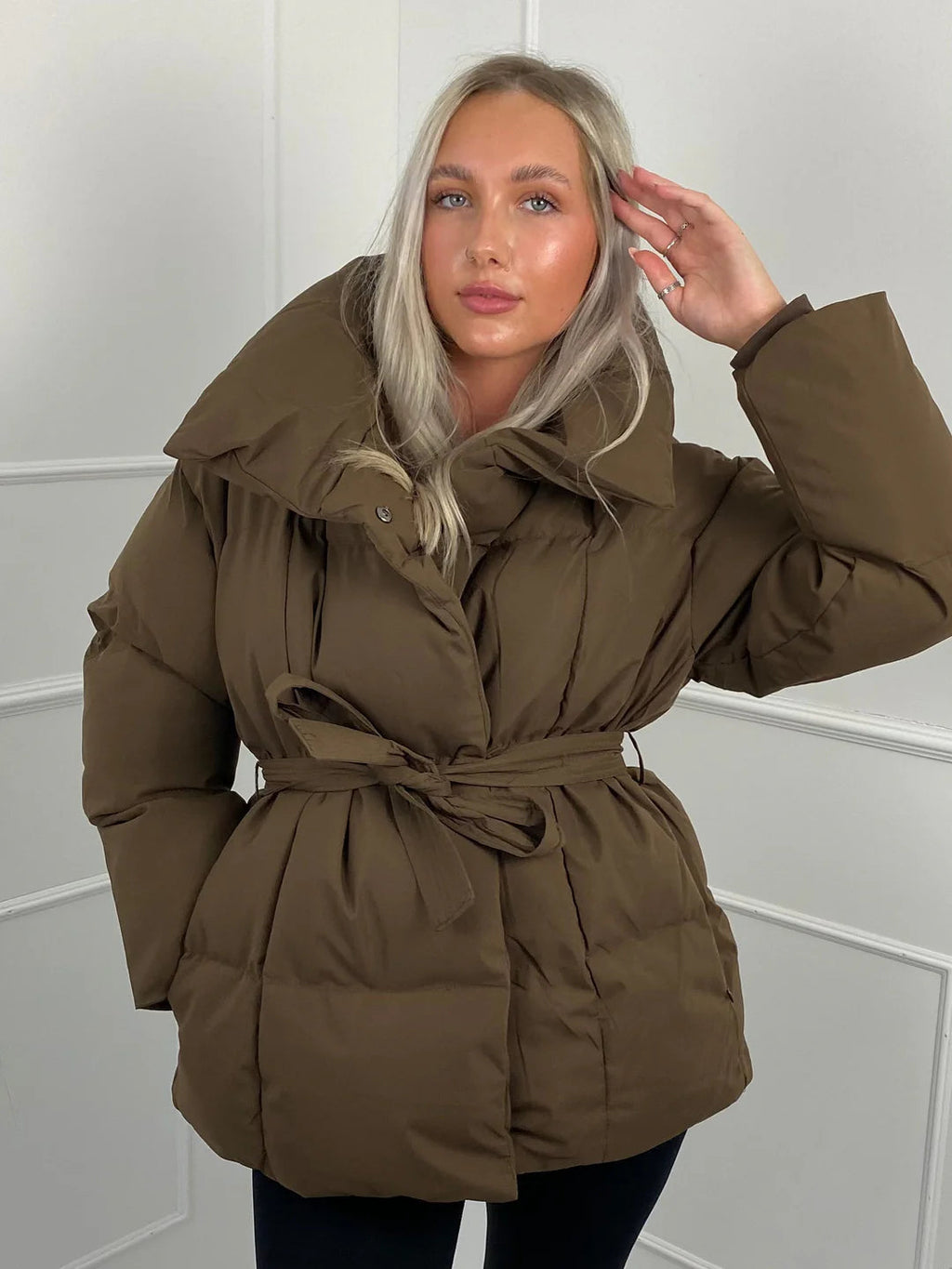 Oversized brown quilted puffer jacket with a high stand collar and a self-tie waist belt for a cinched silhouette.