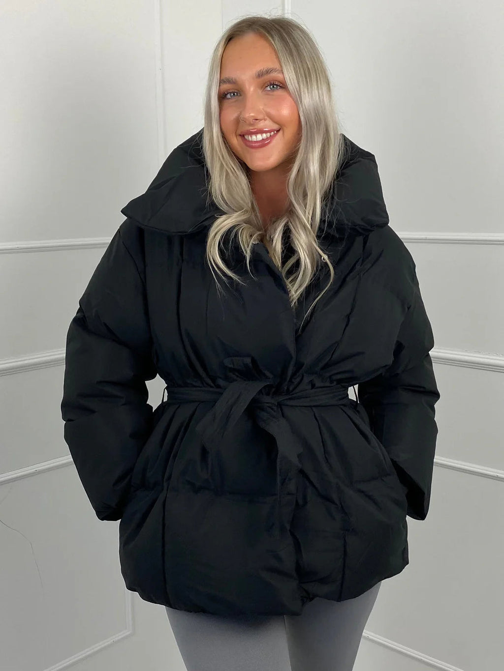 Black quilted puffer jacket with an oversized stand collar and a self-tie waist belt for a cinched, shaped silhouette.