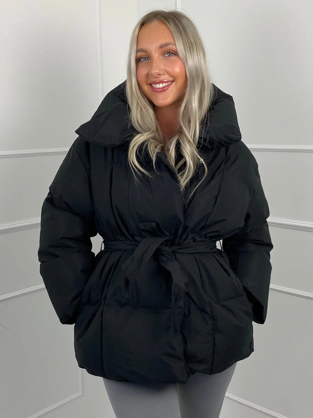Black quilted puffer jacket with an oversized stand collar and a self-tie waist belt for a cinched, shaped silhouette.