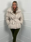 Oversized cream quilted puffer jacket with a high stand collar and a self-tie waist belt for a cinched silhouette.