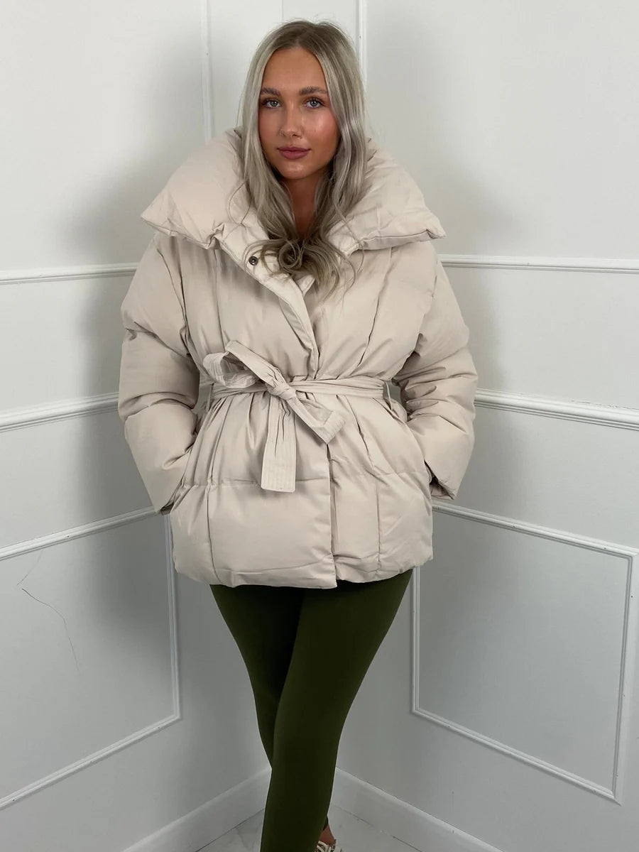 Oversized cream quilted puffer jacket with a high stand collar and a self-tie waist belt for a cinched silhouette.