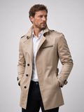 Beige double-breasted trench coat in structured cotton with shoulder epaulettes, cuff straps, and a zip chest pocket.