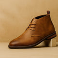 Single tan leather Benjamin chukka boot with lace-up front, propped against a wooden block on tan backdrop