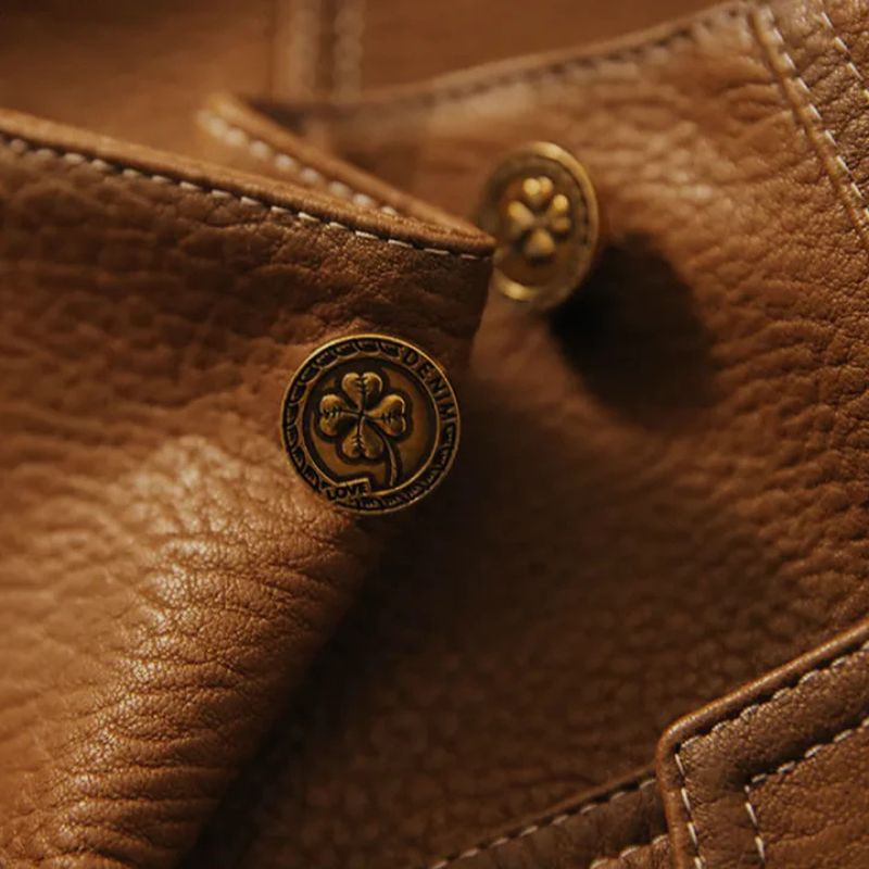 Macro shot of embossed brass snap button and topstitched leather panel showing texture and hardware detail