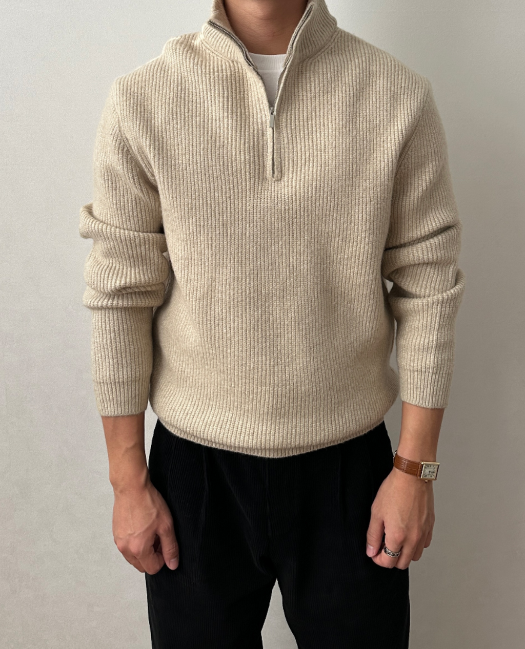 Beige brushed rib-knit quarter-zip sweater with a stand collar and ribbed cuffs, worn over a white tee and black trousers.