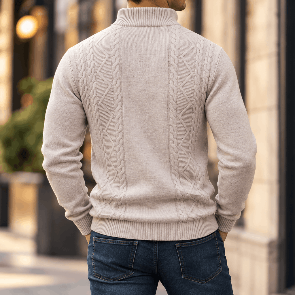 Beige cable-knit quarter-zip sweater with diamond textured panels, ribbed stand collar, and cuffs, worn with dark denim jeans.