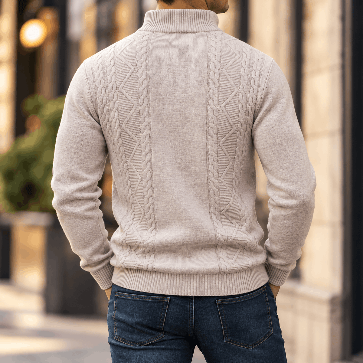 Beige cable-knit quarter-zip sweater with diamond textured panels, ribbed stand collar, and cuffs, worn with dark denim jeans.