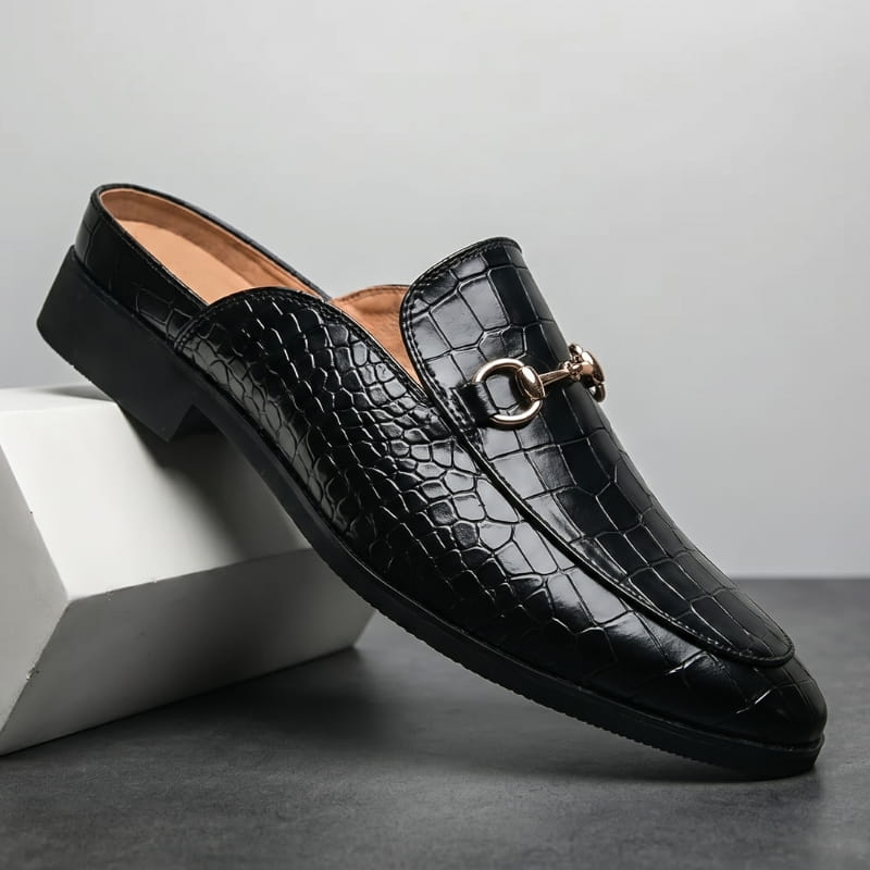 Black croc-embossed leather loafer with gold horsebit buckle propped diagonally against a white geometric block in a studio setting