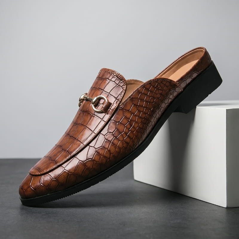 Brown croc-embossed leather loafer with gold horsebit buckle propped diagonally against a white geometric block in a studio setting