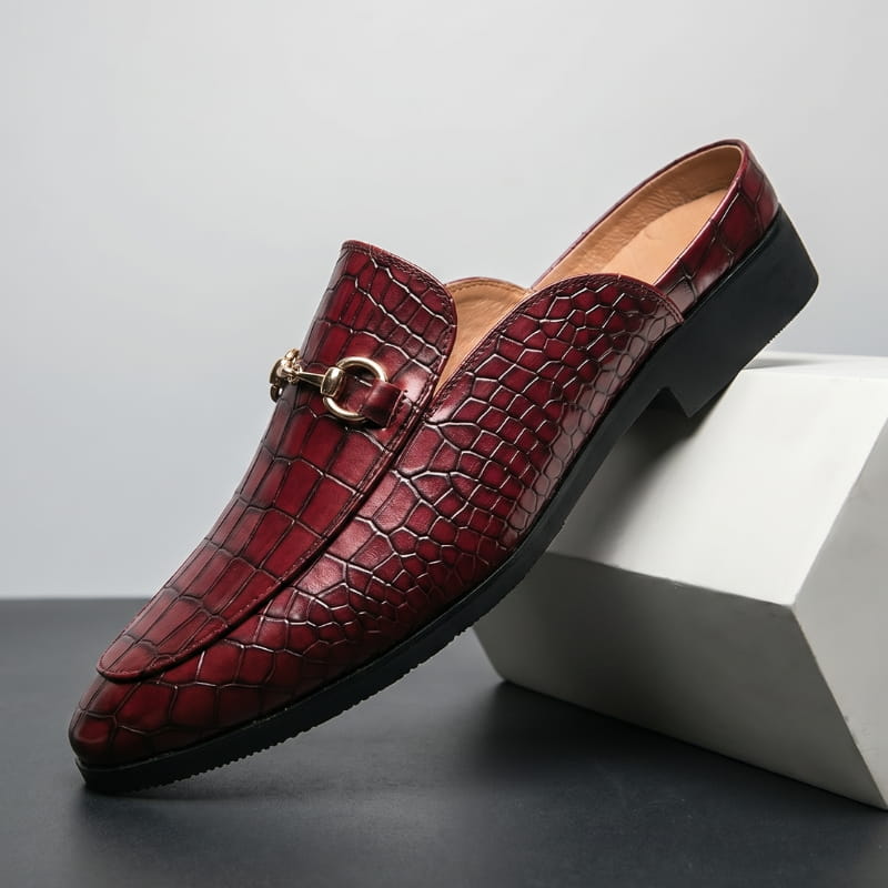 Burgundy croc-embossed leather loafer with gold horsebit buckle propped diagonally against a white geometric block in a studio setting
