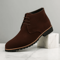 Brown suede chukka boots with lace-up design, cushioned sole, and durable rubber outsole displayed on a white marble pedestal.