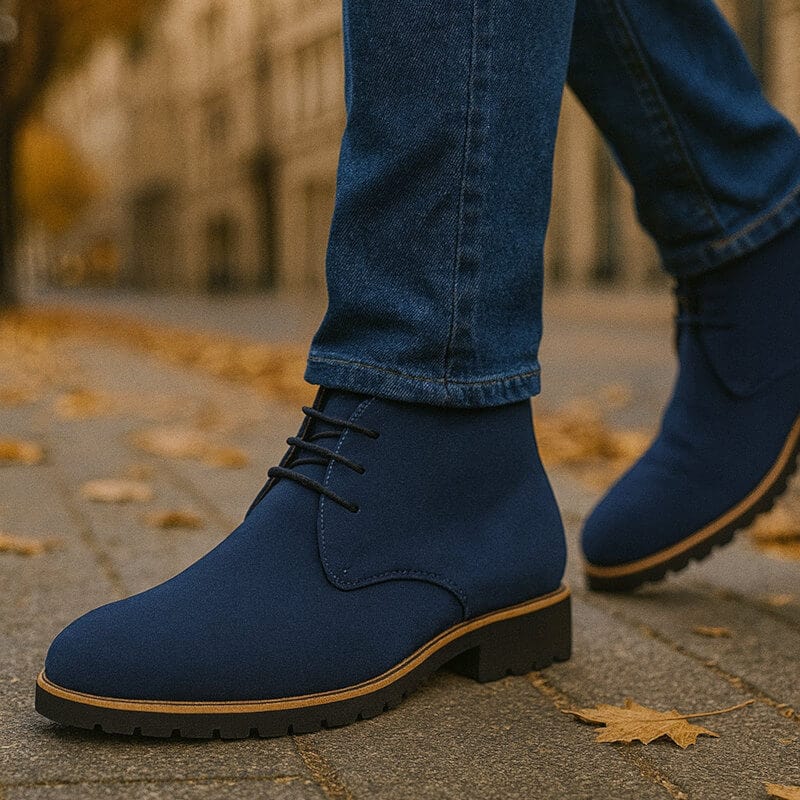 Navy suede chukka boots with lace-up closure and sturdy rubber outsole, styled with blue jeans in an outdoor setting.
