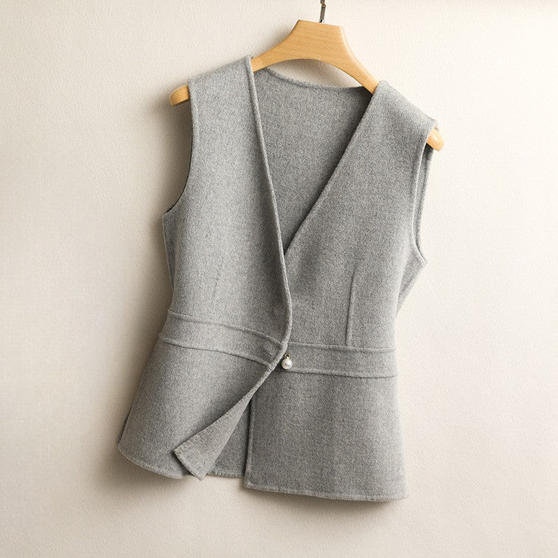 Women's light gray wrap sweater vest with a V-neck, sleeveless silhouette, asymmetric front, peplum hem, and pearl button detail.