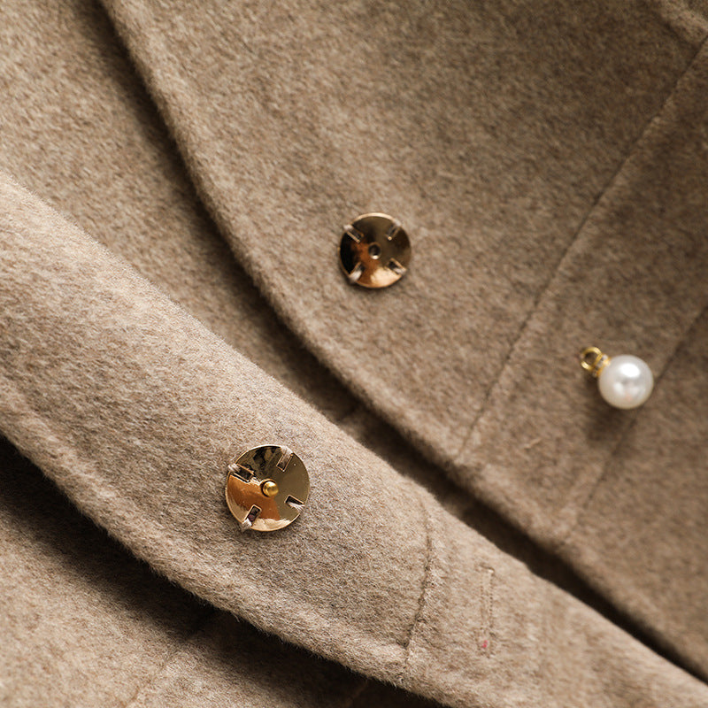 Close-up of the decorative pearl button closure and textured knit fabric on a women's beige wrap sweater vest.