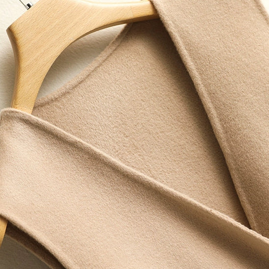 Close-up of the soft beige knit fabric and wrap edge on a women's sleeveless peplum sweater vest.
