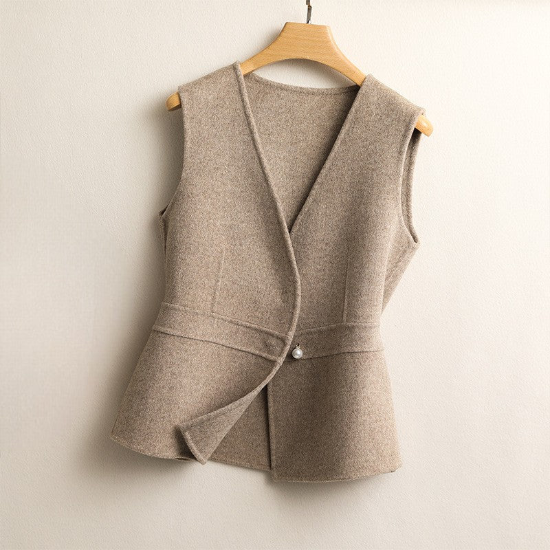 Women's beige wrap sweater vest featuring a V-neck, sleeveless design, asymmetric front, peplum hem, and decorative pearl button closure.
