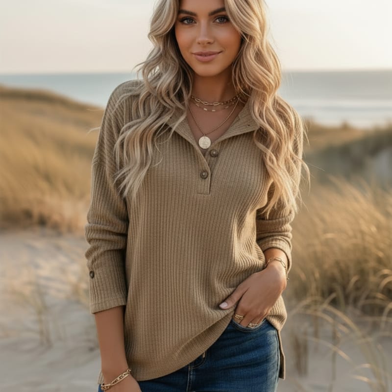 Woman wearing a khaki waffle knit Henley sweater with a collared button neckline, long sleeves, and a relaxed fit in a beachside setting.