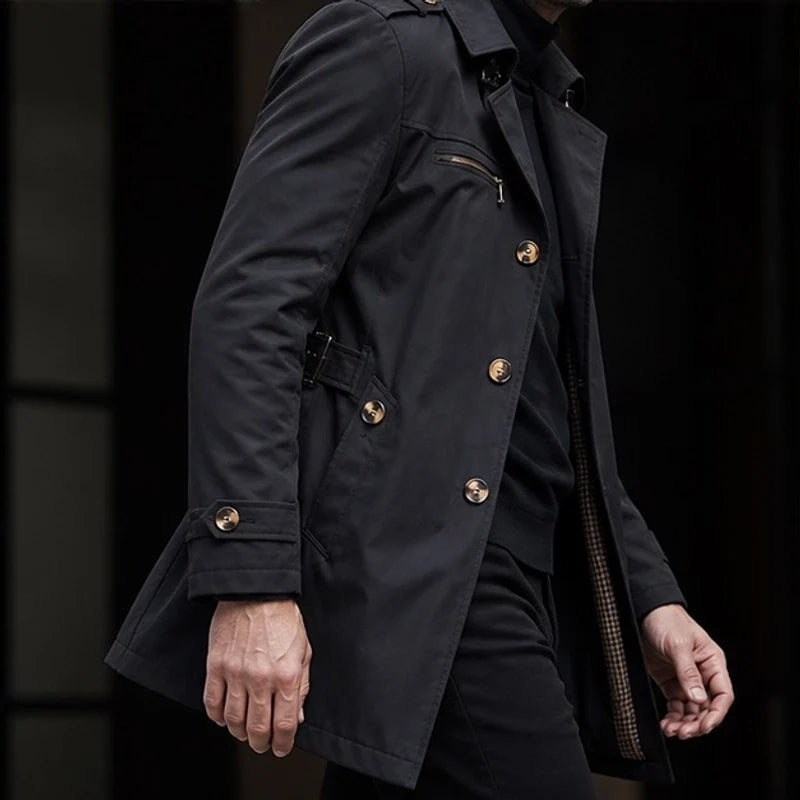 Black cotton-blend trench coat with button front, zip chest pocket, and buckled cuff straps in a structured silhouette.