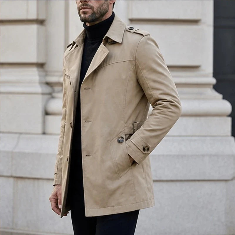Beige cotton-blend trench coat with notched lapels, shoulder epaulettes, and a button-front closure over a black turtleneck.