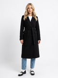 Black wool-blend longline trench coat with a belted waist, notched lapels, and double-breasted fit over blue jeans.